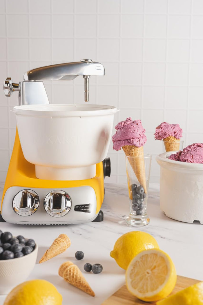 Ice cream maker in a yellow blender next to ice cream and fruit displayed on a kitchen countertop