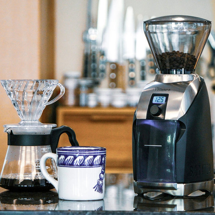 Baratza Virtuoso+ Burr Coffee Grinder next to a coffee dripper station and mug on a countertop