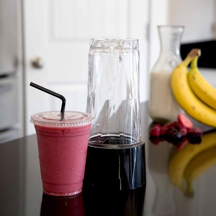 Blendtec GO Travel Cup next to a plastic cup with pink smoothie on a kitchen countertop with fruit and milk in the background
