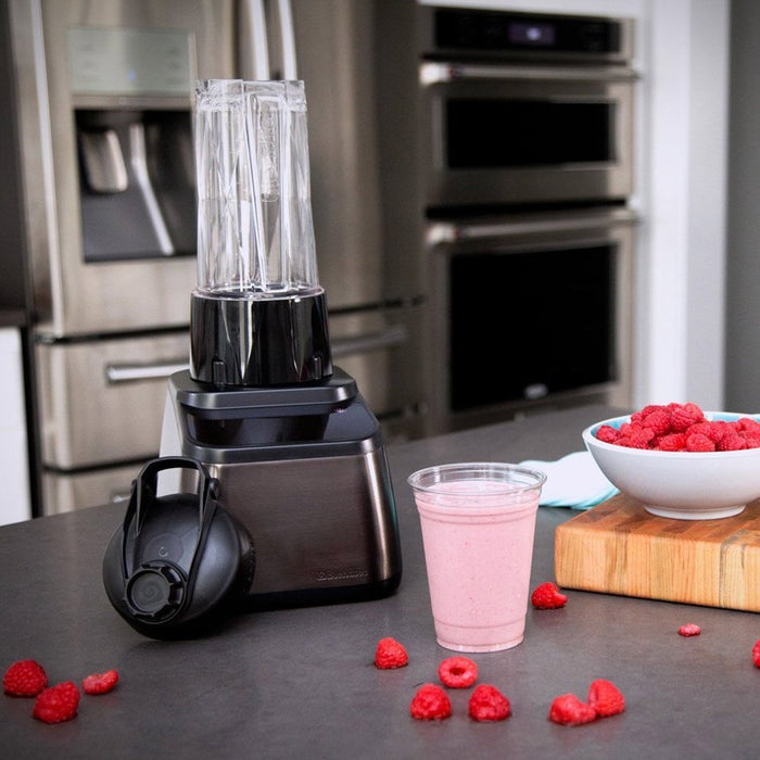 Blendtec GO Travel Cup with a plastic cup with pink smoothie next to raspberries in a kitchen setting