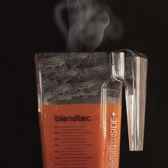 Close up of steaming red liquid inside a Blendtec blender displayed on a black background
