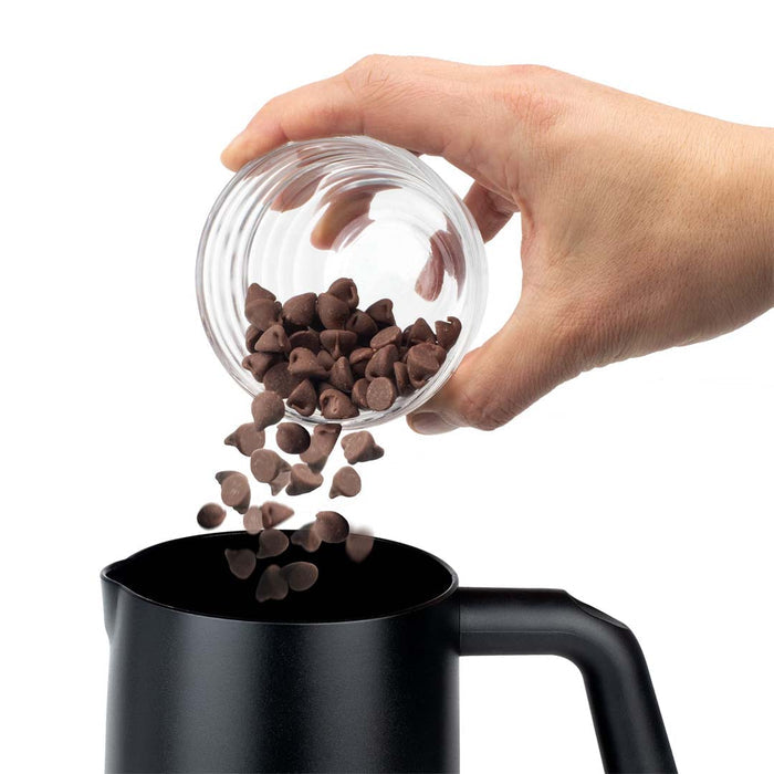 Someone pouring chocolate chips inside black Capresso automatic milk frother displayed on a white background