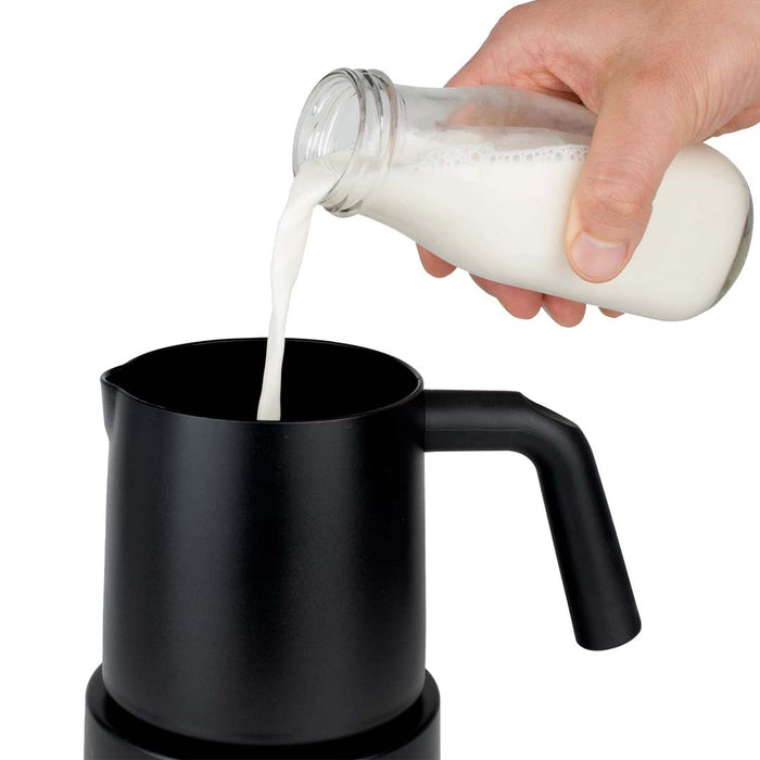 Someone pouring milk in black Capresso automatic milk frother displayed on a white background