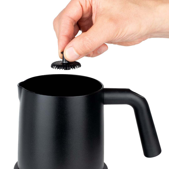 Someone holding a part above black Capresso automatic milk frother displayed on a white background