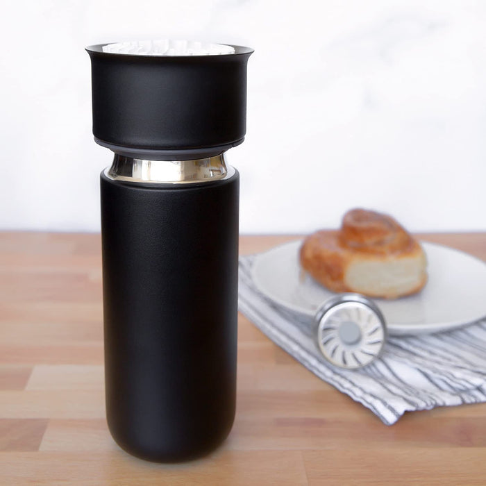 Black tumblr on a wooden surface with a plate of bread in the background