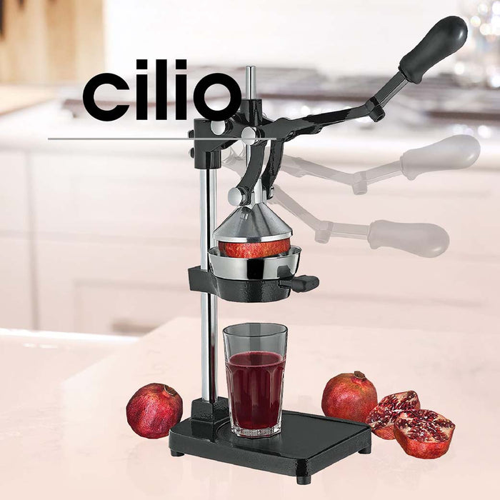 Frieling black Cilio juicer extractor and juice press with a cup full of pomegranate juice and pomegranates while one is being juiced displayed on a blurred kitchen background