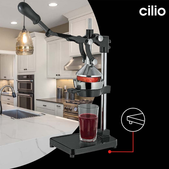Frieling black Cilio juicer extractor and juice press with a cup full of pomegranate juice and pomegranates while one is being juiced displayed on black background and a kitchen setting