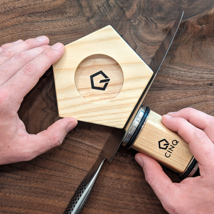 Someone demonstrating on how to use Cinq Knife Sharpening tool on a wooden surface