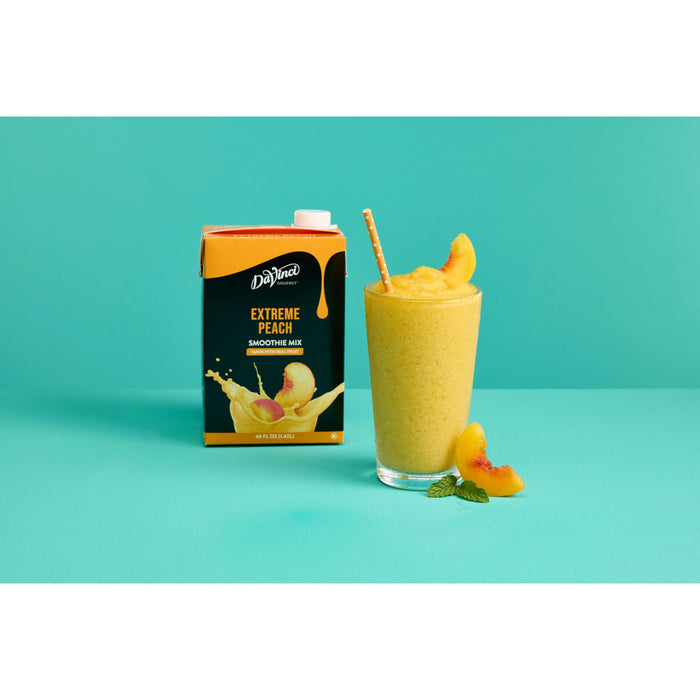Glass cup with fruit smoothie with peach slices and straw next to Davinci Extreme Peach smoothie mix on an aqua and white background
