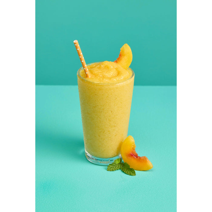 Glass cup with fruit smoothie mix with peach slices and straw on an aqua and white background