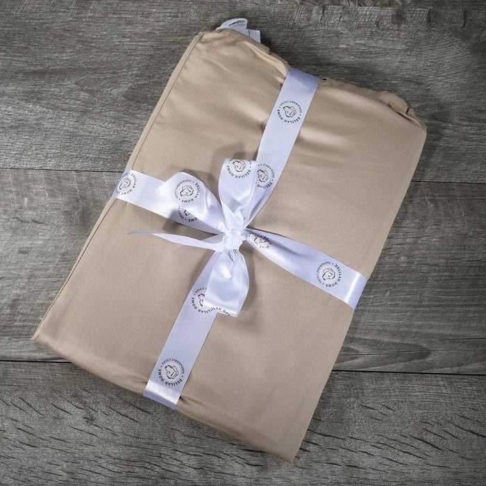 Top view of a folded beige queen Delilah home 100 organic cotton bed sheet set tied with a ribbon, on a wooden surface.