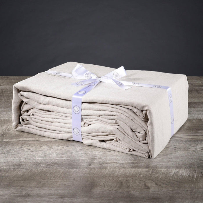 A folded natural twin XL Delilah Home 100 organic Hemp Bed Sheet set tied with a ribbon, displayed on a wooden surface.