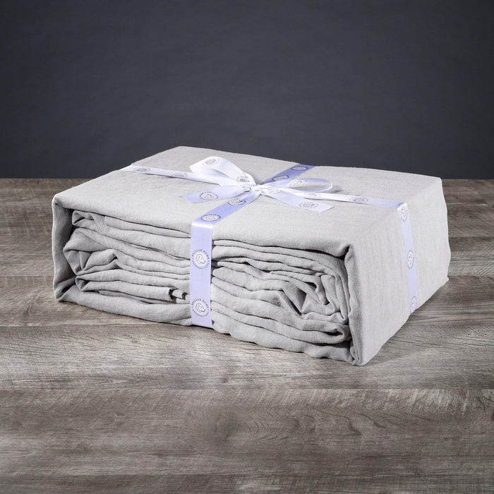 A folded light gray twin XL Delilah Home 100 organic Hemp Bed Sheet set tied with a ribbon, displayed on a wooden surface.