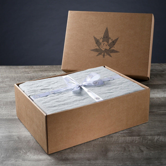 A folded mineral green twin XL Delilah Home 100 organic Hemp Bed Sheet set tied with a ribbon, displayed in packaging on a wooden surface.