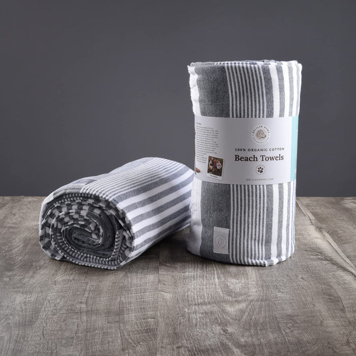 Two blue Delilah Home beach towels on a wooden surface and grey background