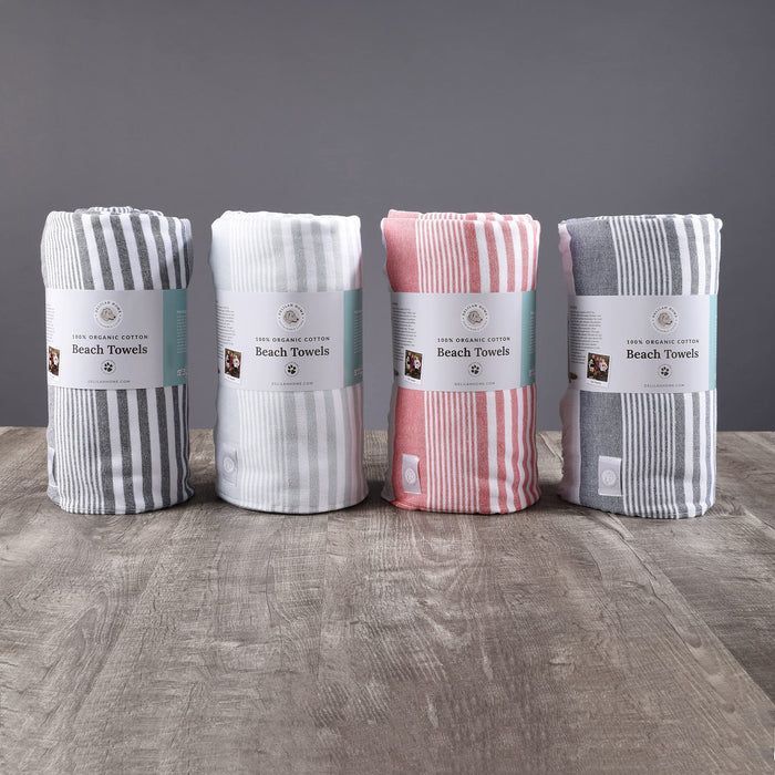 Four different colored Delilah Home beach towels placed on a wooden surface with a grey background
