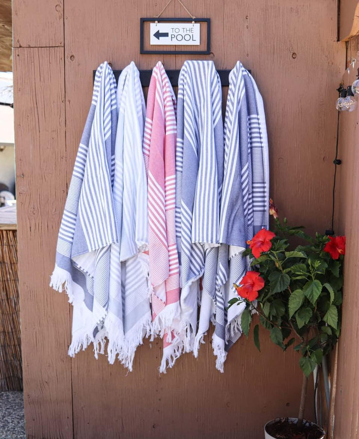 Different colored beach towels hanging on coat hooks on a wooden panel next to a flower plant