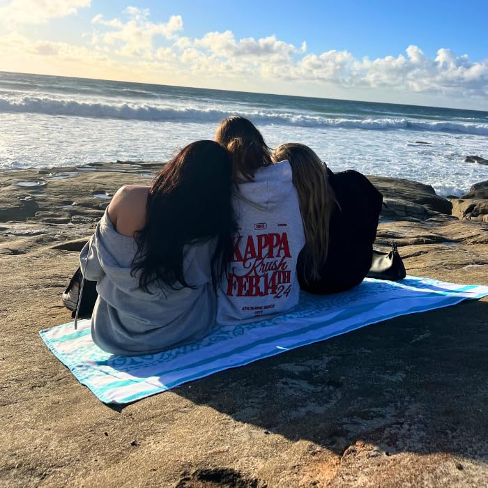 Three individuals sitting on light blue Delilah home beach towel on the beach looking out into the ocean