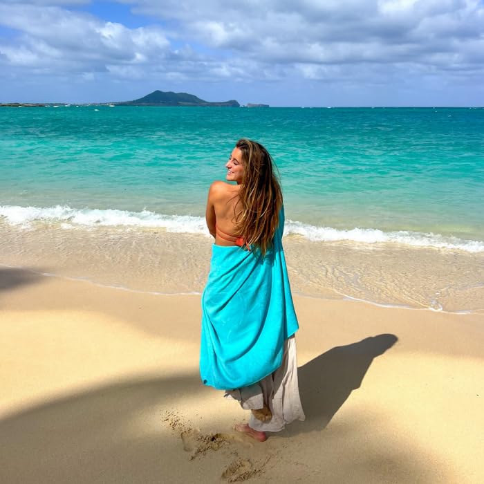 A young lady with light blue Delilah home beach towel wrapped around her on the beach with the ocean and mountain in the background