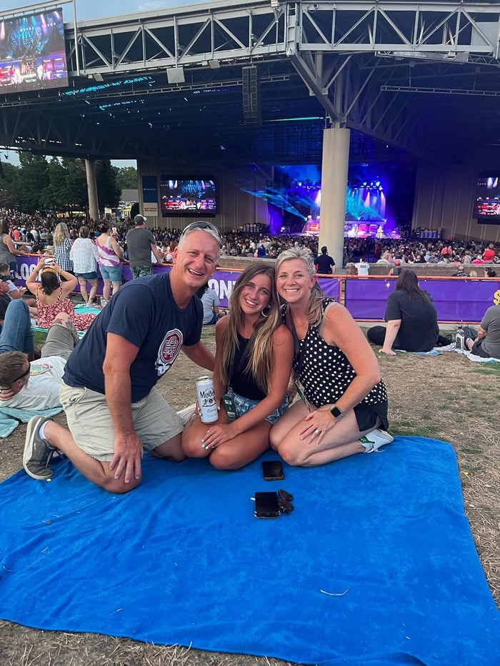 Three individuals using a Delilah home beach towel at a concert