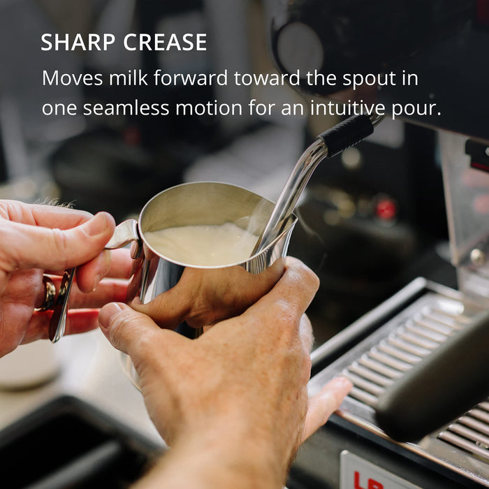 Person holding a metal milk steaming pitcher with milk, preparing to steam it with a coffee machine.
