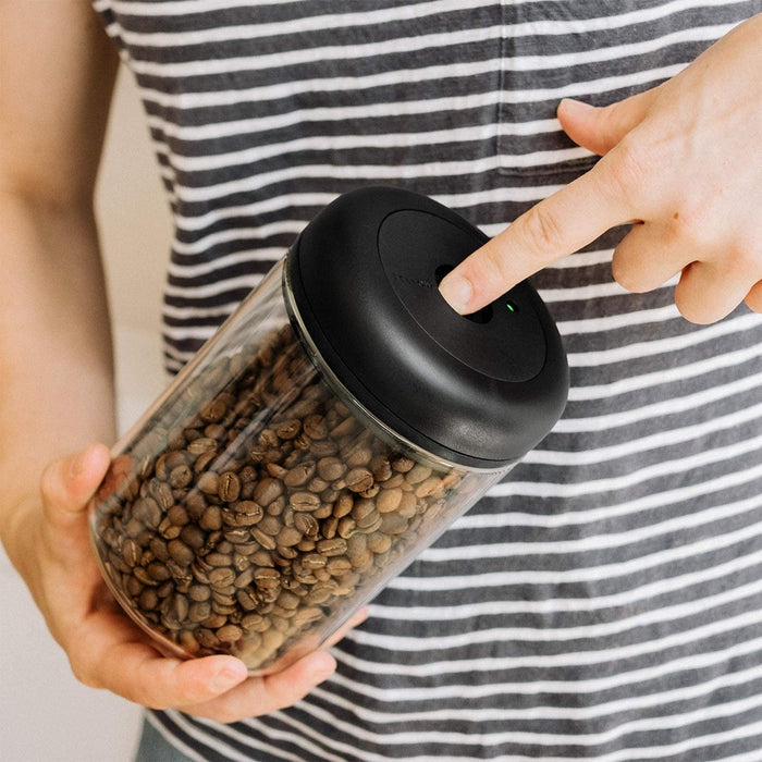 Person holding a jar of coffee beans with a black lid