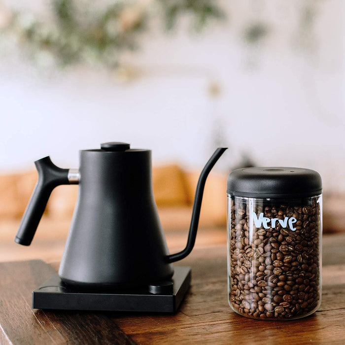 Black coffee kettle and jar of coffee beans on a wooden surface with a blurred background