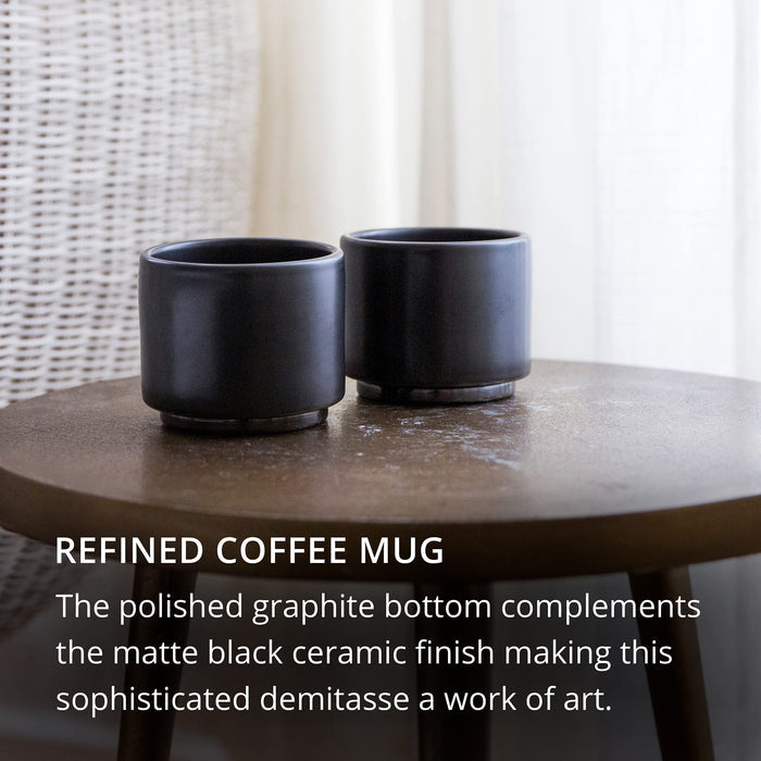 Two matte black ceramic coffee mugs on a wooden table with text describing the product.
