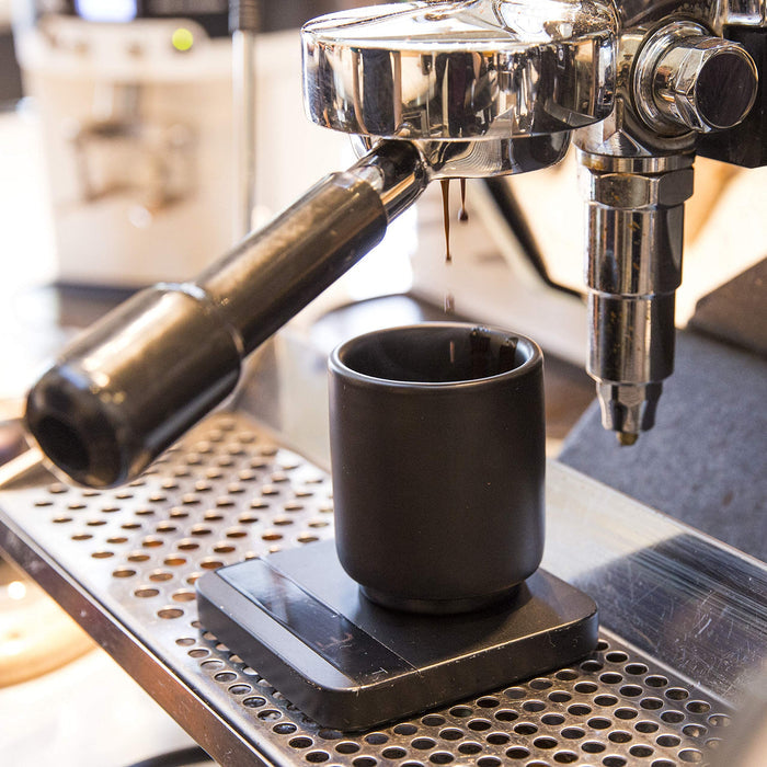 Espresso machine dispensing coffee into a black cup on a metal surface.