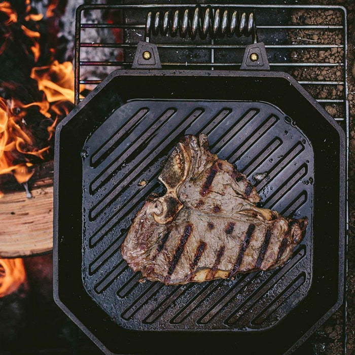 FINEX 12″ Cast Iron Grill Pan displayed on a fireplace grilling a steak