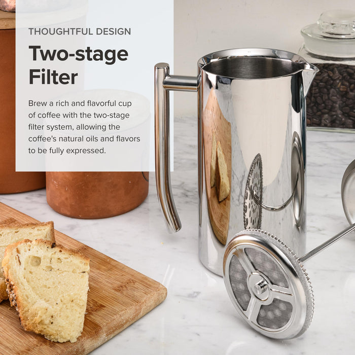 Silver French press coffee maker with a two-stage filter on a marble surface with bread and jars.