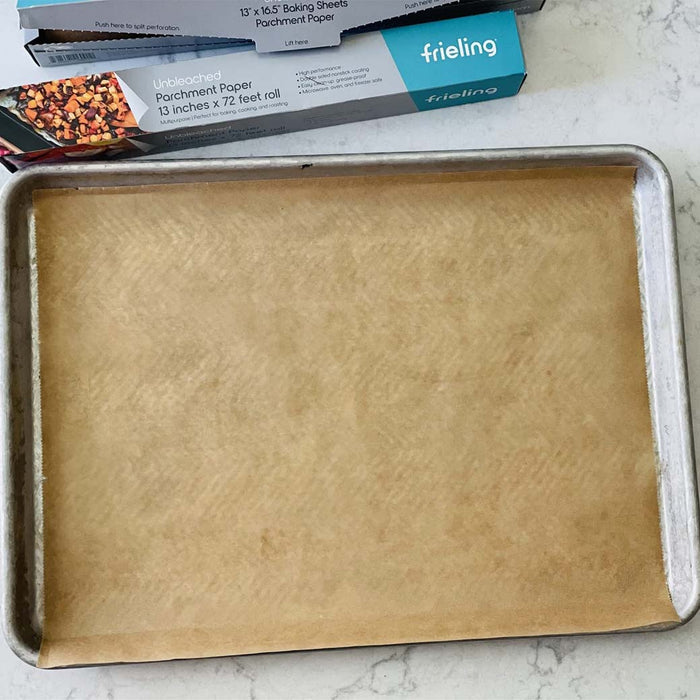 Frieling unbleached parchment paper on a baking sheet placed on a marble countertop next to parchment packaging