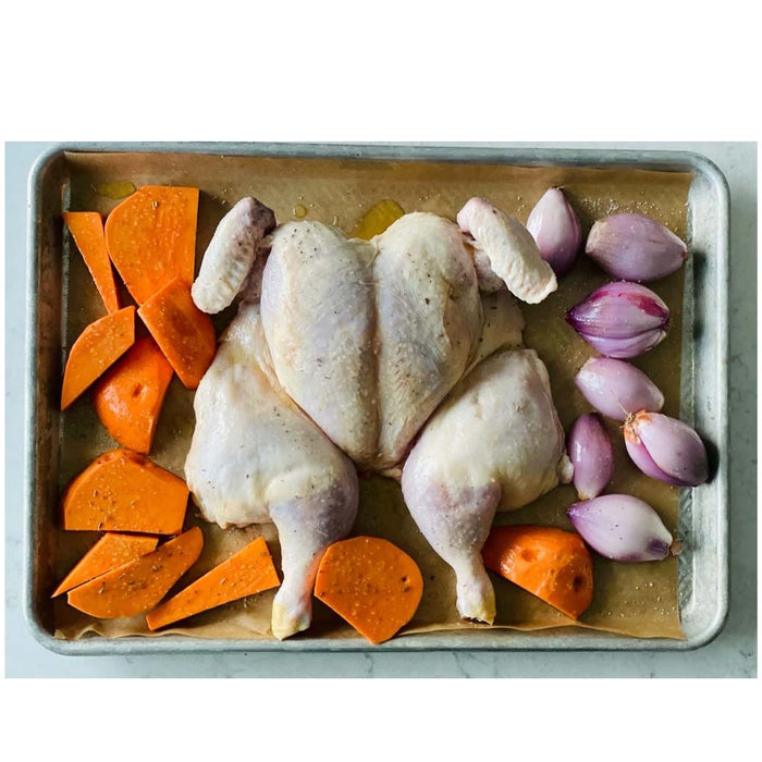 Chicken, potato, and shallots on Frieling unbleached parchment paper placed on a baking sheet on a marble countertop