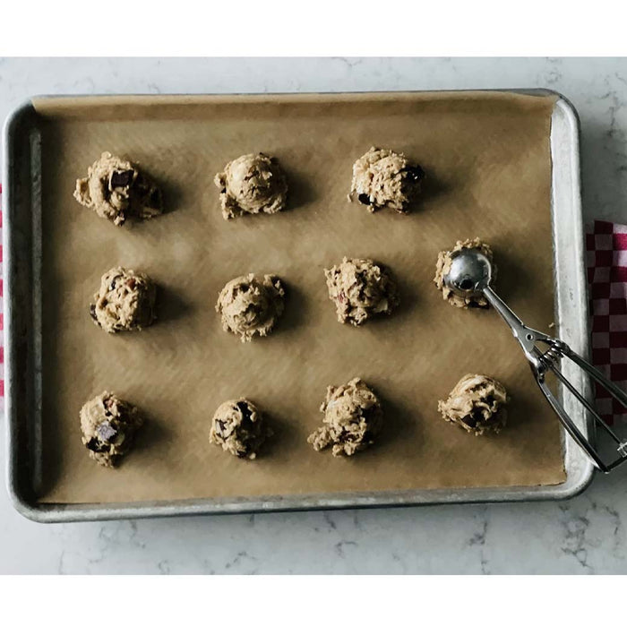 A baking sheet with Frieling unbleached parchment paper with cookie mix balls on the parchment paper placed on marble countertop