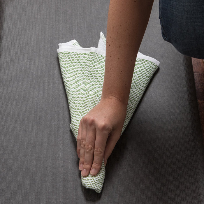 Someone using a table cloth to clean a Gelpro designer comfort anti fatigue kitchen floor mat