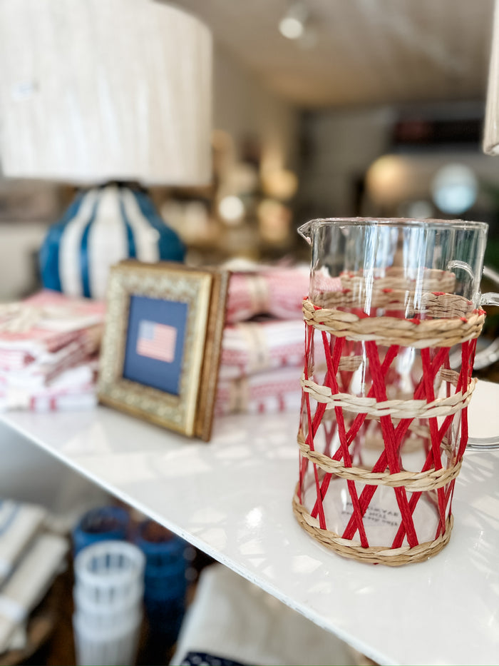 Glass pitcher with woven sleeve.