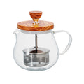 Clear glass teapot with wooden lid and handle on a white background
