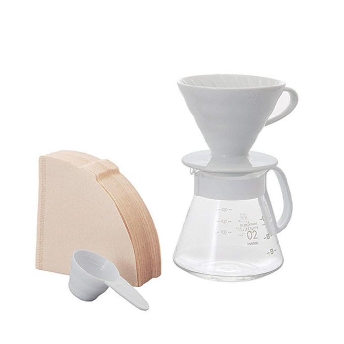 White ceramic Hario dripper on a carafe next to filters and white measurement scoop displayed on a white background