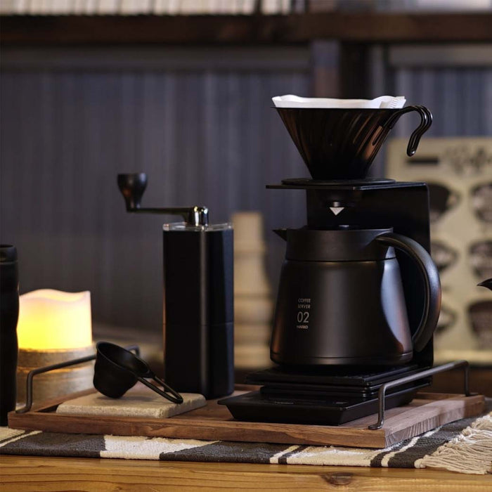 Matte black Hario V60 coffee dripper on a coffee setup on a wooden table