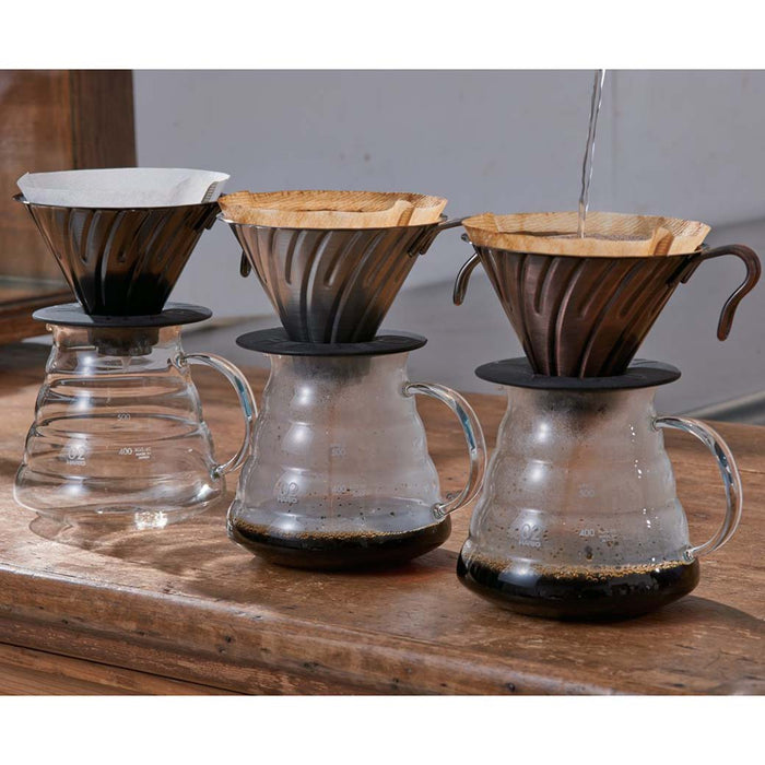Set of 3 Hario V60 coffee dripper with someone pouring water into one displayed on a wooden surface