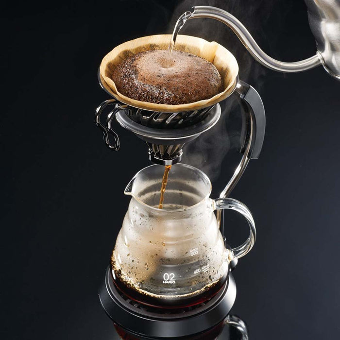 Water being poured into a Hario V60 coffee dripper which is dripping coffee into a carafe displayed on a black background