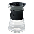 Clear glass drip decanter with black silicone sleeve on a white background