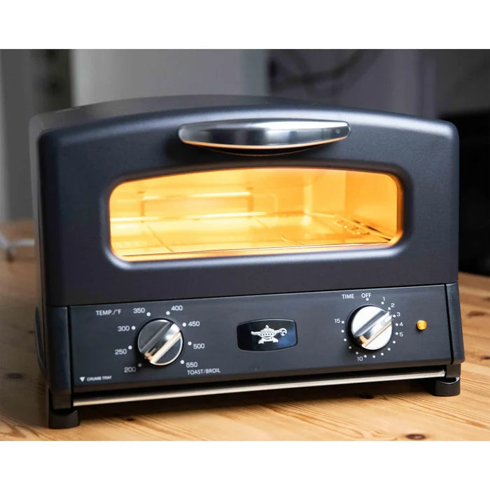 Matte black toaster oven turned on with knobs displayed on a wooden surface