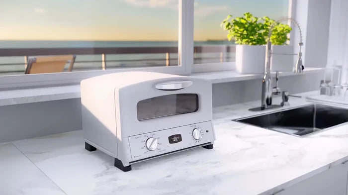 Modern white toaster oven on a kitchen counter with a view of the ocean.