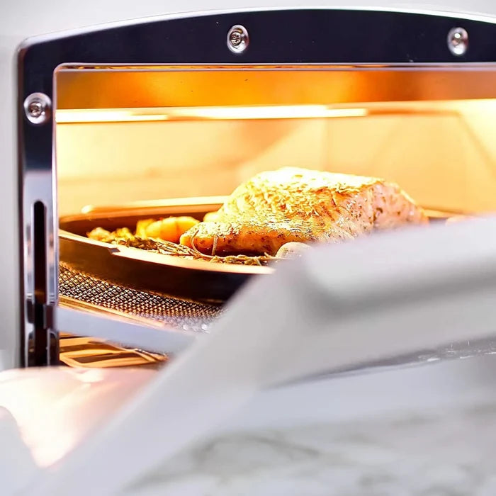 A close-up view inside a toaster oven, with a piece of salmon cooking under a warm orange light on a baking tray. The oven door is slightly open in the foreground.