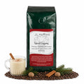 1 lb J.L. Hufford Spiced Eggnog coffee bag with coffee beans, glass of eggnog, pine needles, and cinnamon sticks on a white background