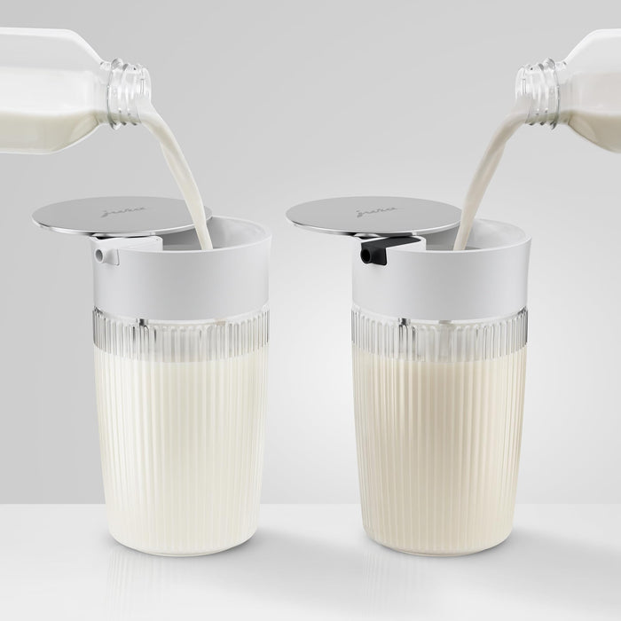 Two Jura 16.9oz glass milk carafe with lid with milk being poured into both on a white surface and background