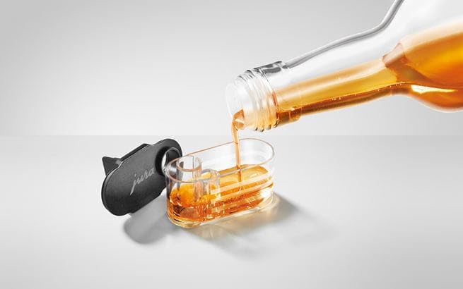 A close-up image of the JURA syrup attachment having syrup being poured into it on a white background