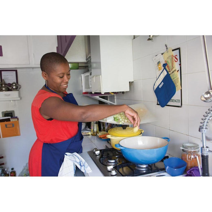 An individual pouring veggies into Le Creuset 1 qt Enameled Cast Iron Signature Oval Dutch Oven, Sand Interior in a kitchen setting
