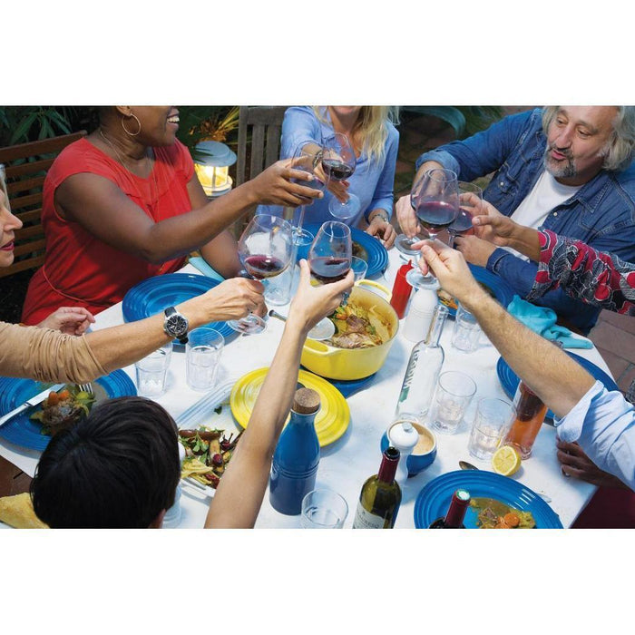 People cheersing at a dinner table with an assortment of Le Creuset cookware and dinnerware